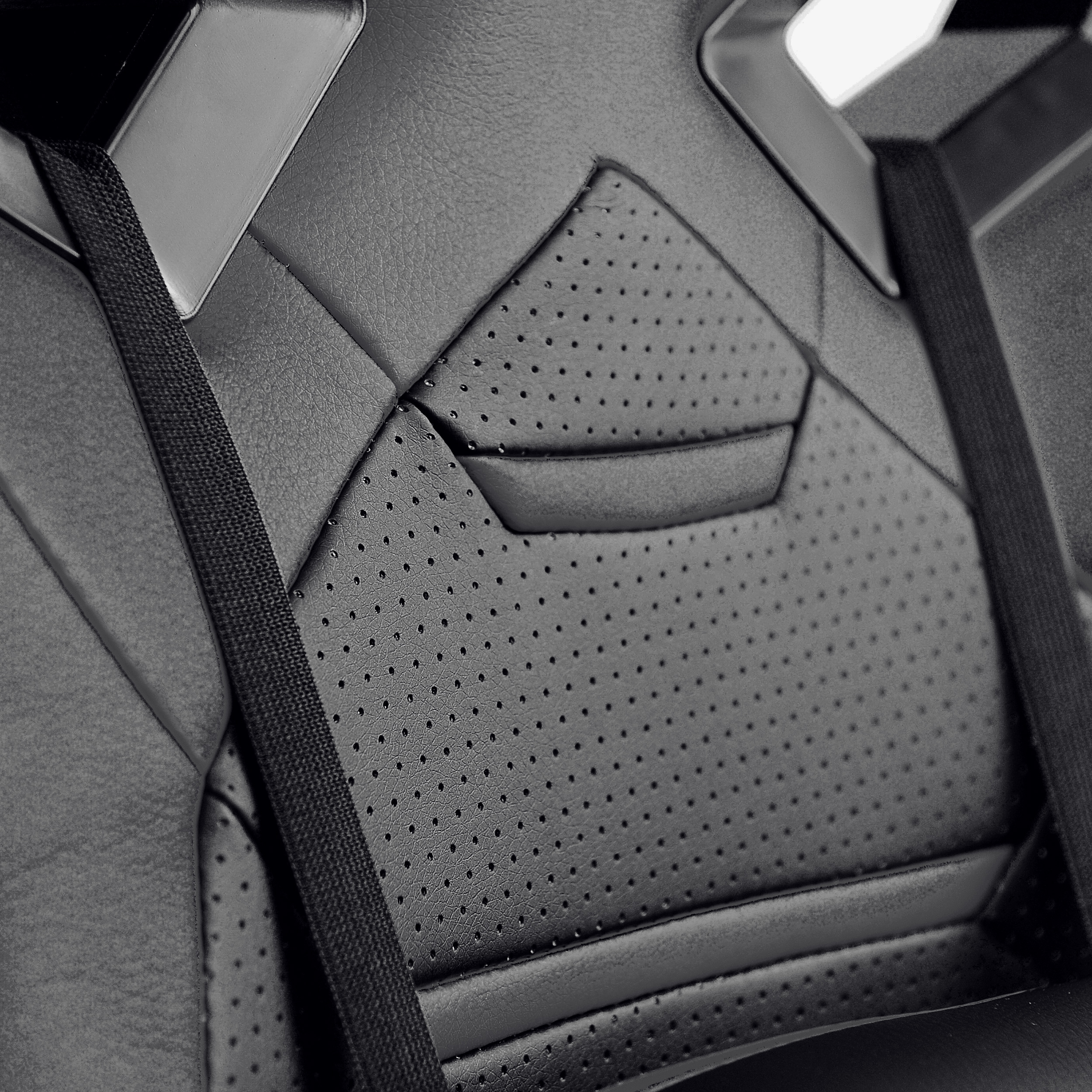 Czarny skórzany fotel samochodowy z perforowanym wzorem i paskami pasów bezpieczeństwa.