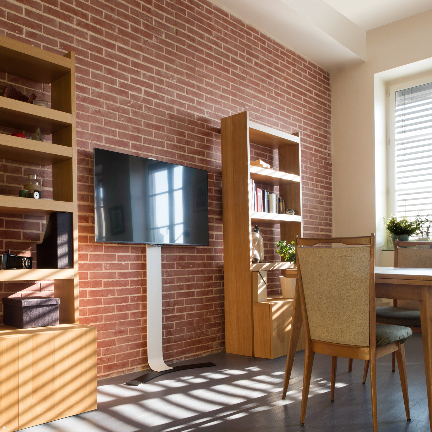 Soggiorno con muro in mattoni, TV su supporto, scaffali e mobili in legno. Finestra con persiane.