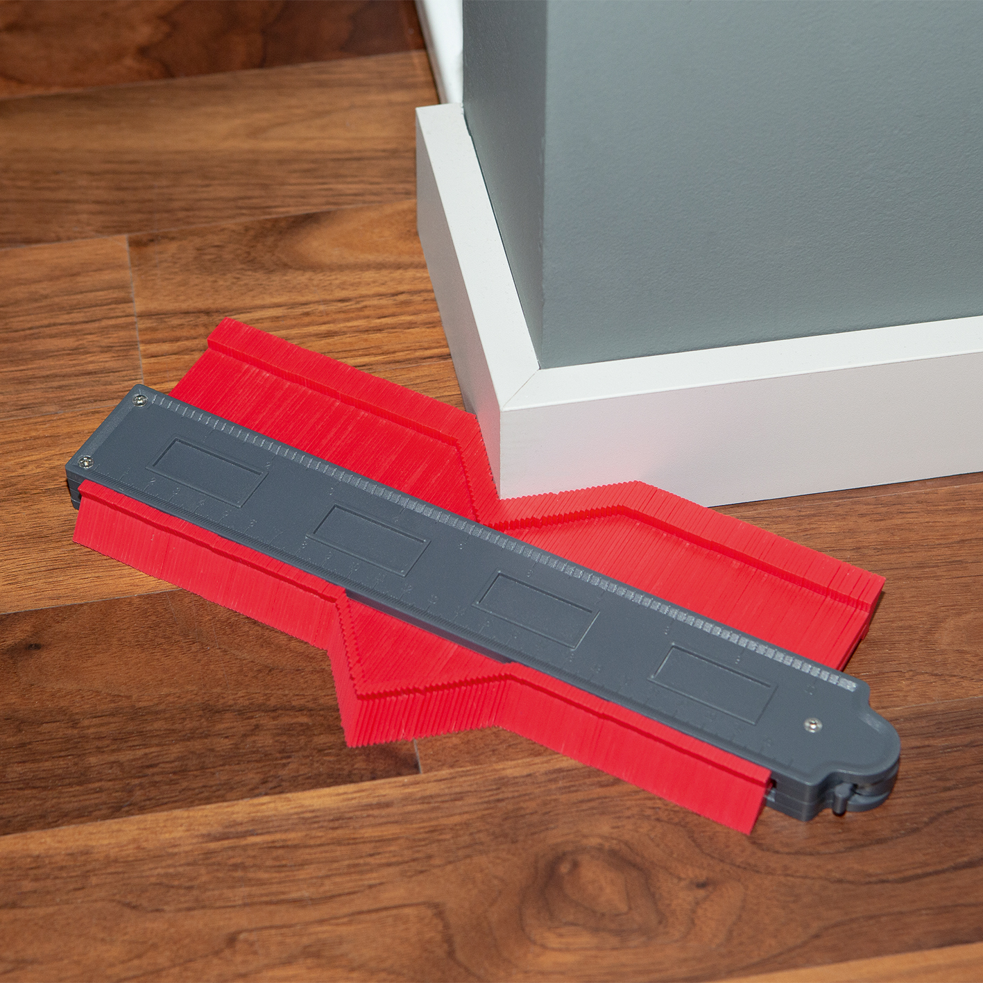Rotes und graues Eckmesswerkzeug auf Holzboden neben weißer und grauer Wand.