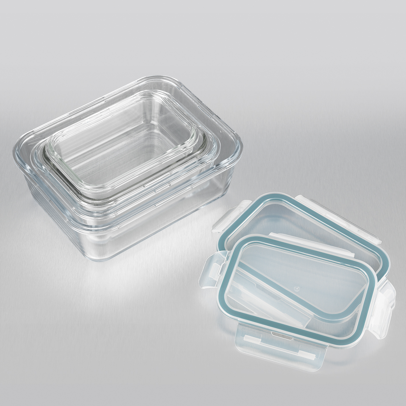Drei transparente Glasbehälter mit Deckeln, gestapelt und offen, auf einer Metalloberfläche.