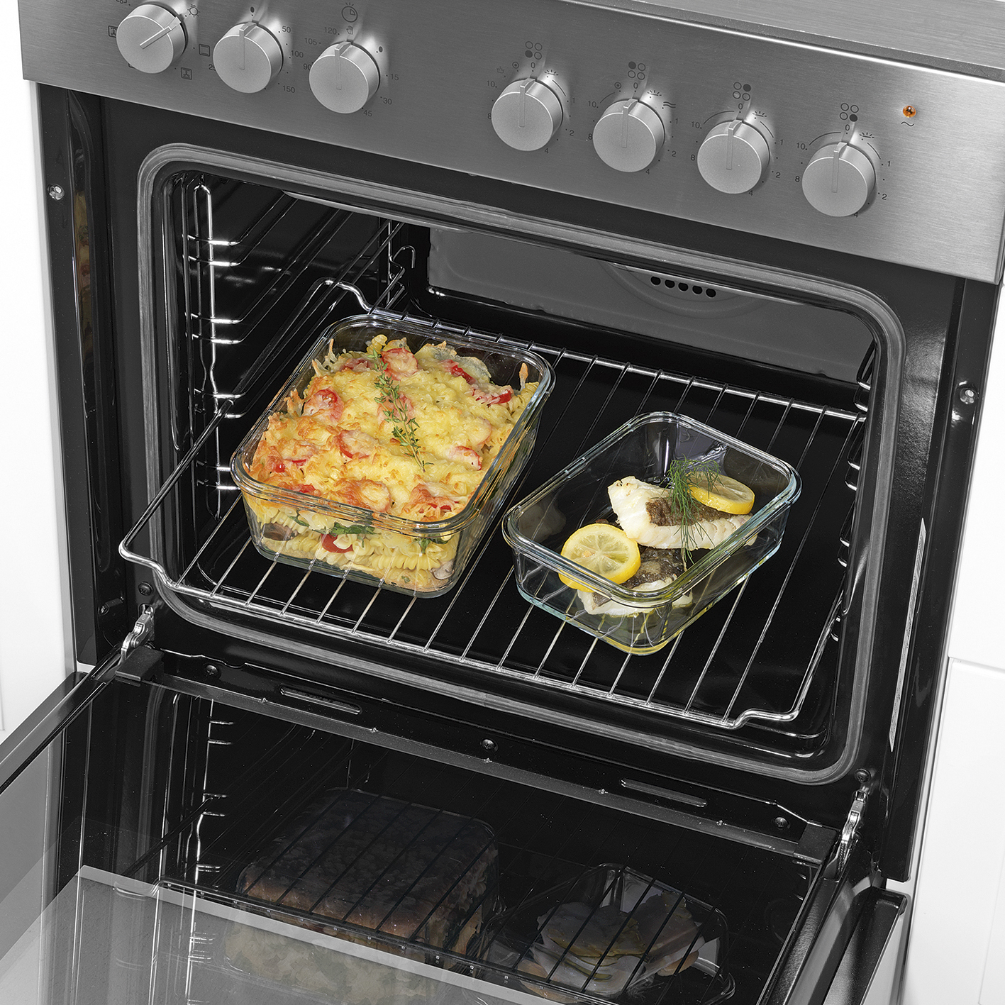Ofen mit zwei Glasformen. Eine mit Pasta und Garnelen, die andere mit Fisch und Zitrone.