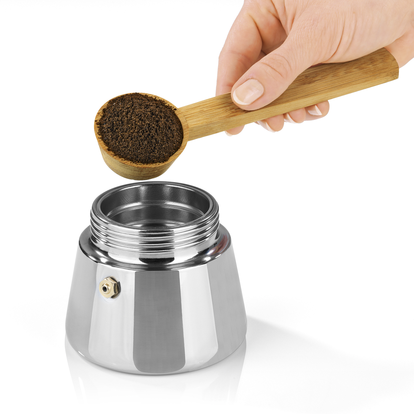 Eine Hand schüttet Kaffeepulver von einem Holzlöffel in einen Espressokocher aus Edelstahl.