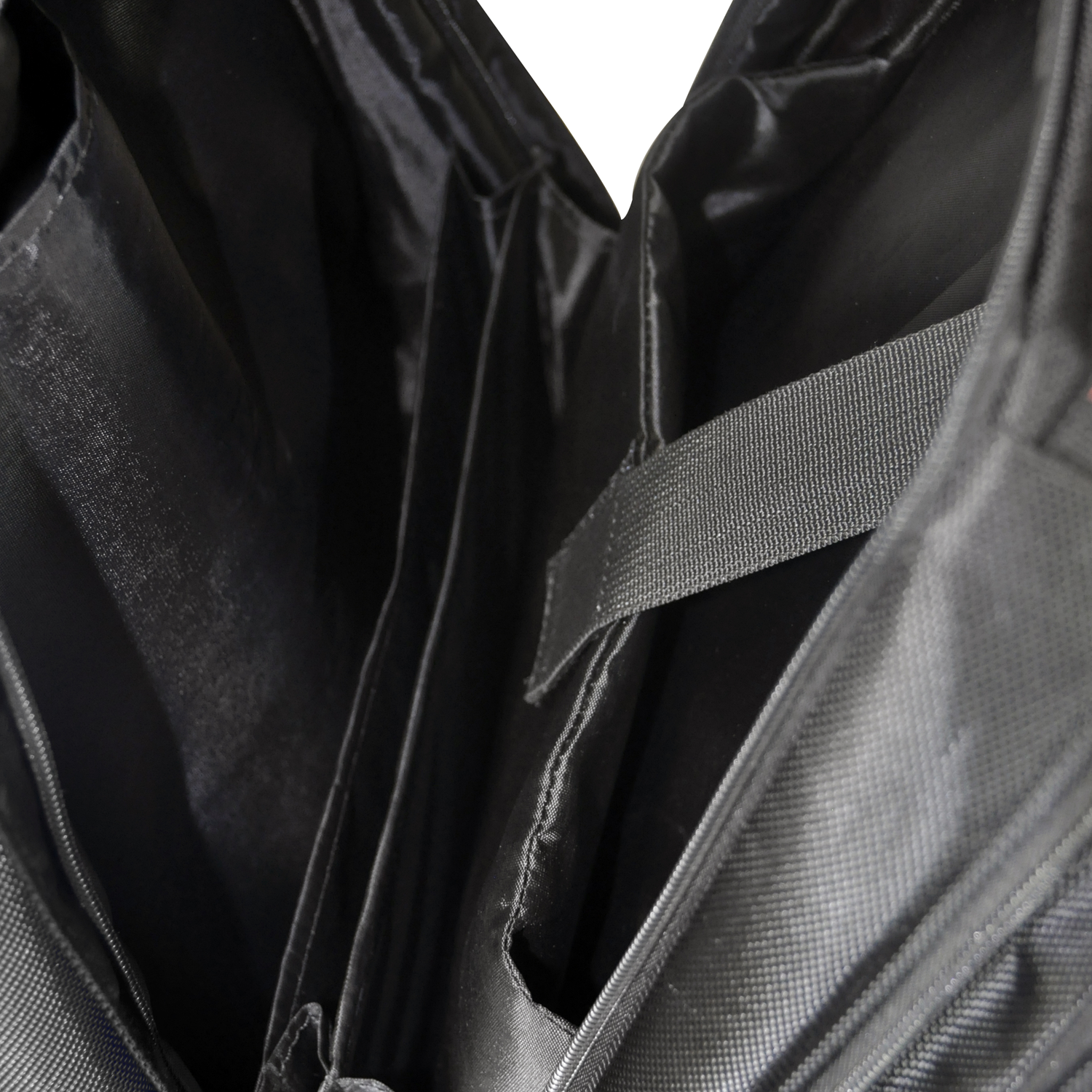 Borsa nera aperta con scomparti. Tasche interne e cinturino nero su superficie bianca.