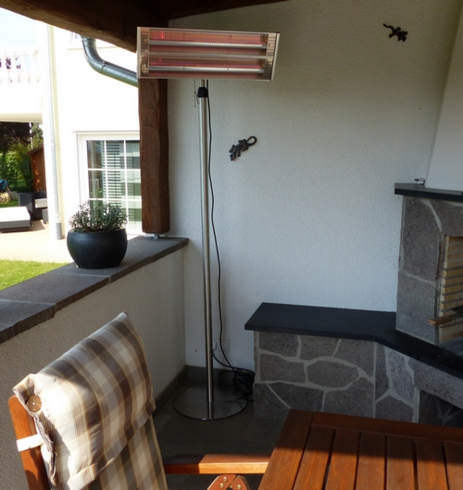 Ein Heizstrahler auf einer Terrasse, mit Tisch und Stuhl im Vordergrund.