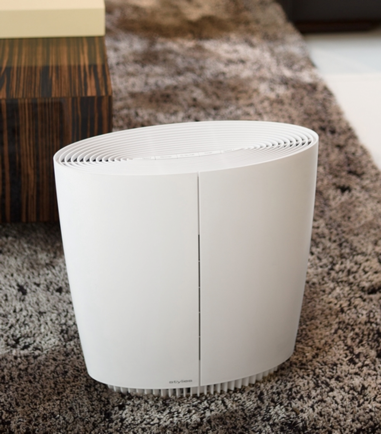 Un purificatore d'aria bianco e cilindrico è su un tappeto fantasia. Un mobile in legno è sfocato sullo sfondo.
