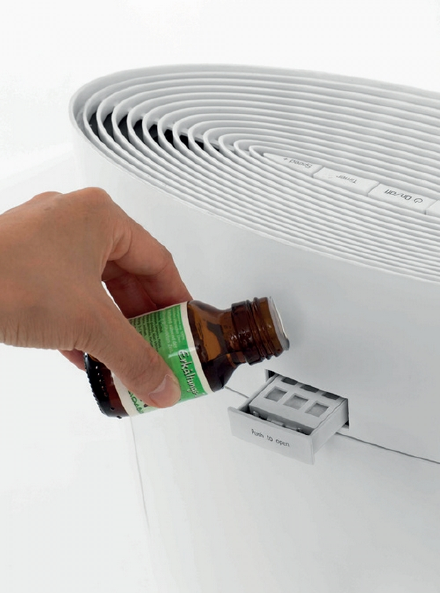 Una mano versa olio da una bottiglia marrone in un purificatore d'aria bianco.