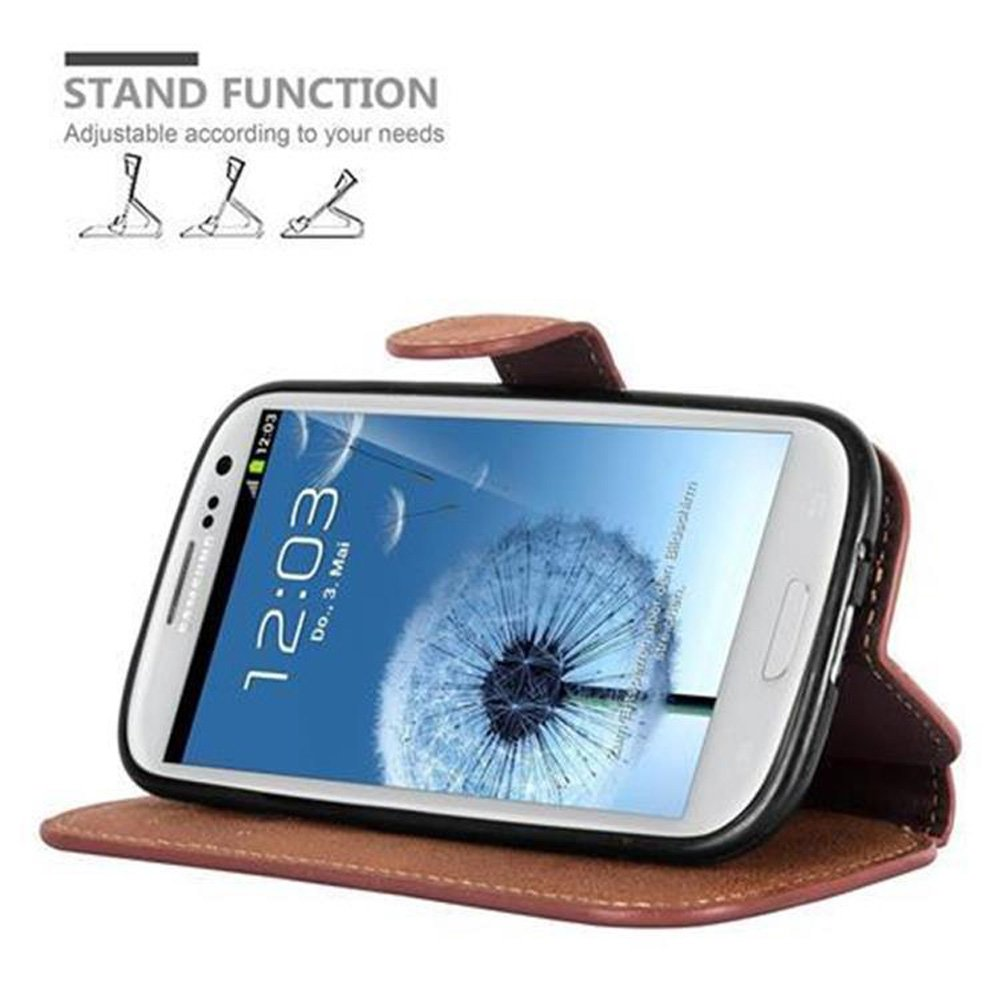 Un teléfono en una funda tipo cartera, apoyado para que se mantenga de pie. El fondo es blanco.