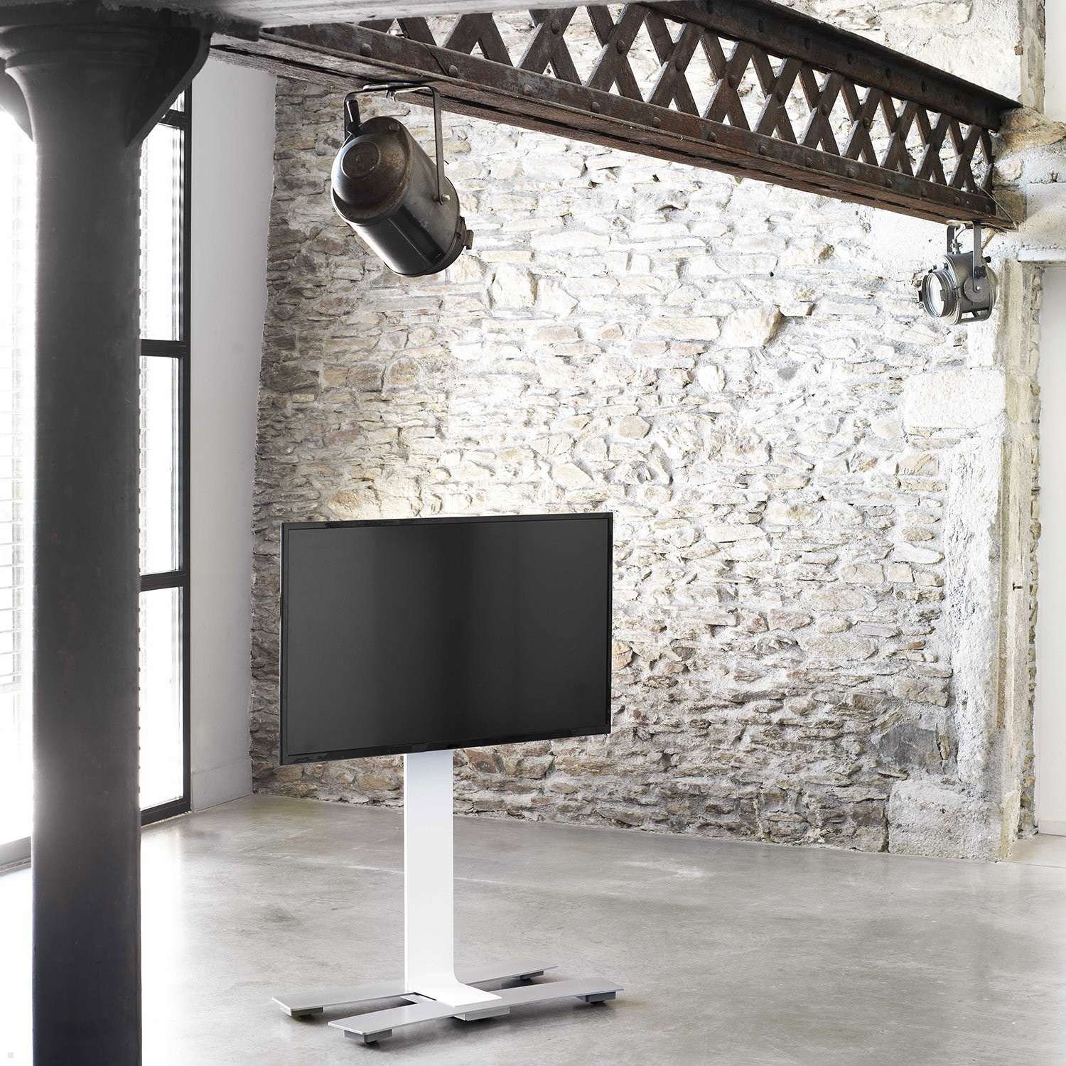 Modernes Interieur mit großem Fernseher auf weißem Ständer. Sichtbare Backsteinmauer und dunkle Decke.