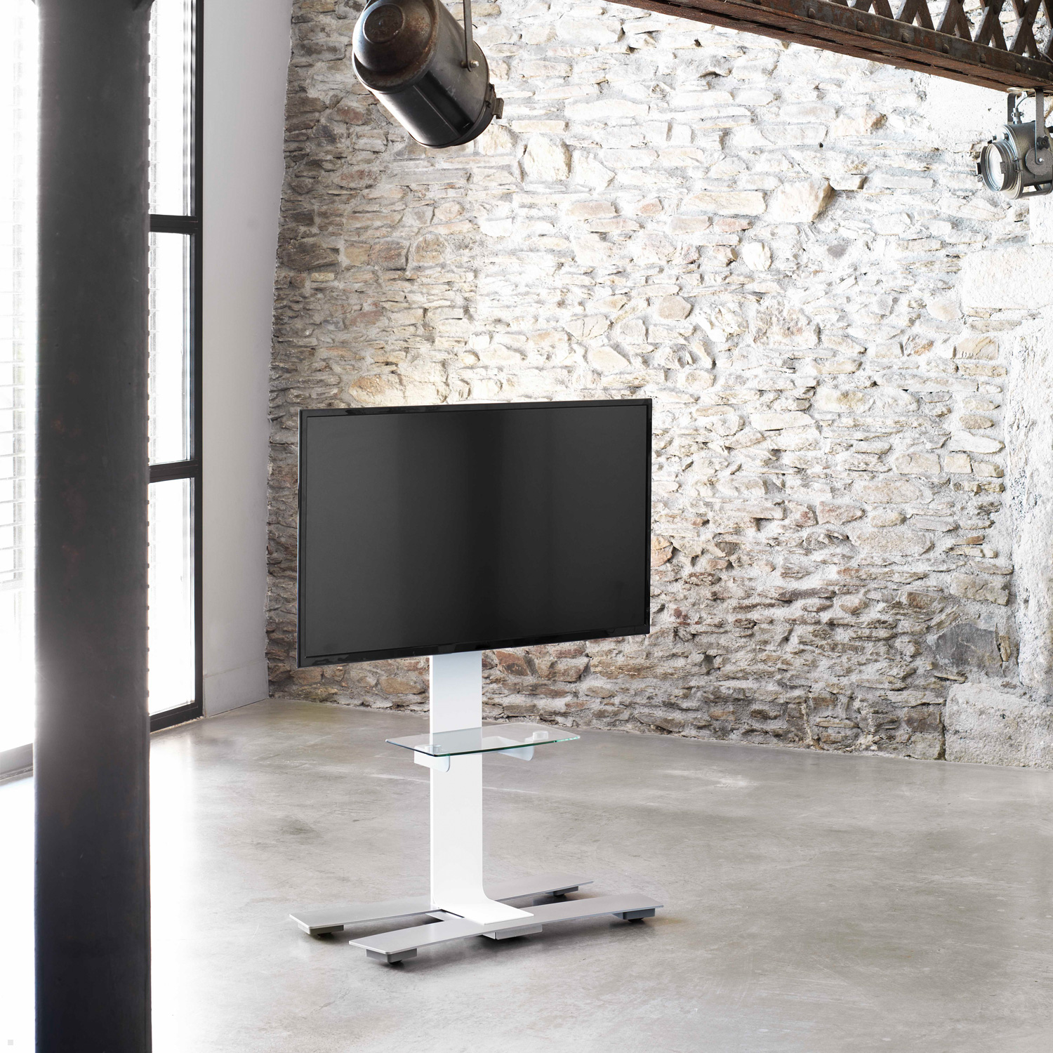 Moderner TV-Ständer mit schwarzem Bildschirm in einem Raum mit Steinmauer und Betonboden.