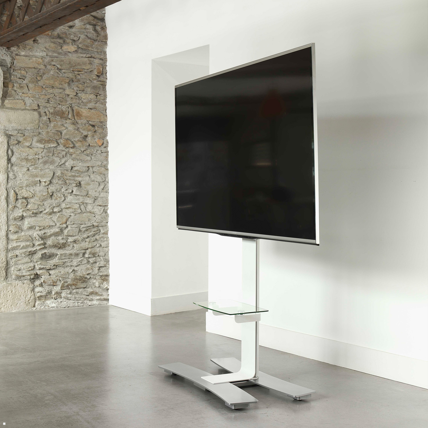 Ein großer Fernseher auf einem weißen Ständer, in einem Raum mit Steinmauer und glänzendem Boden.