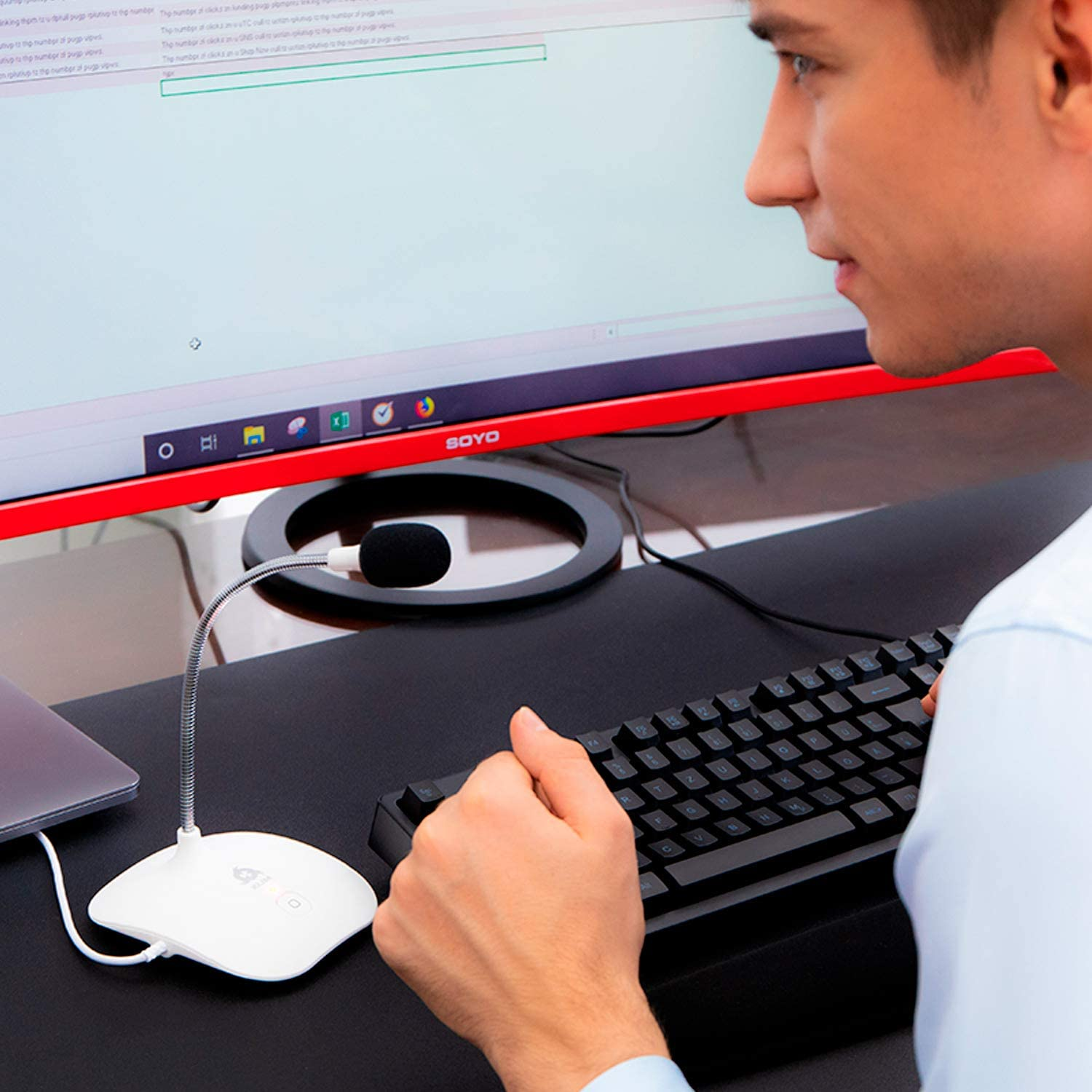 Mann nutzt Computer mit Mikrofon, Monitor, Tastatur. Schwarzer Tisch, roter Monitor.