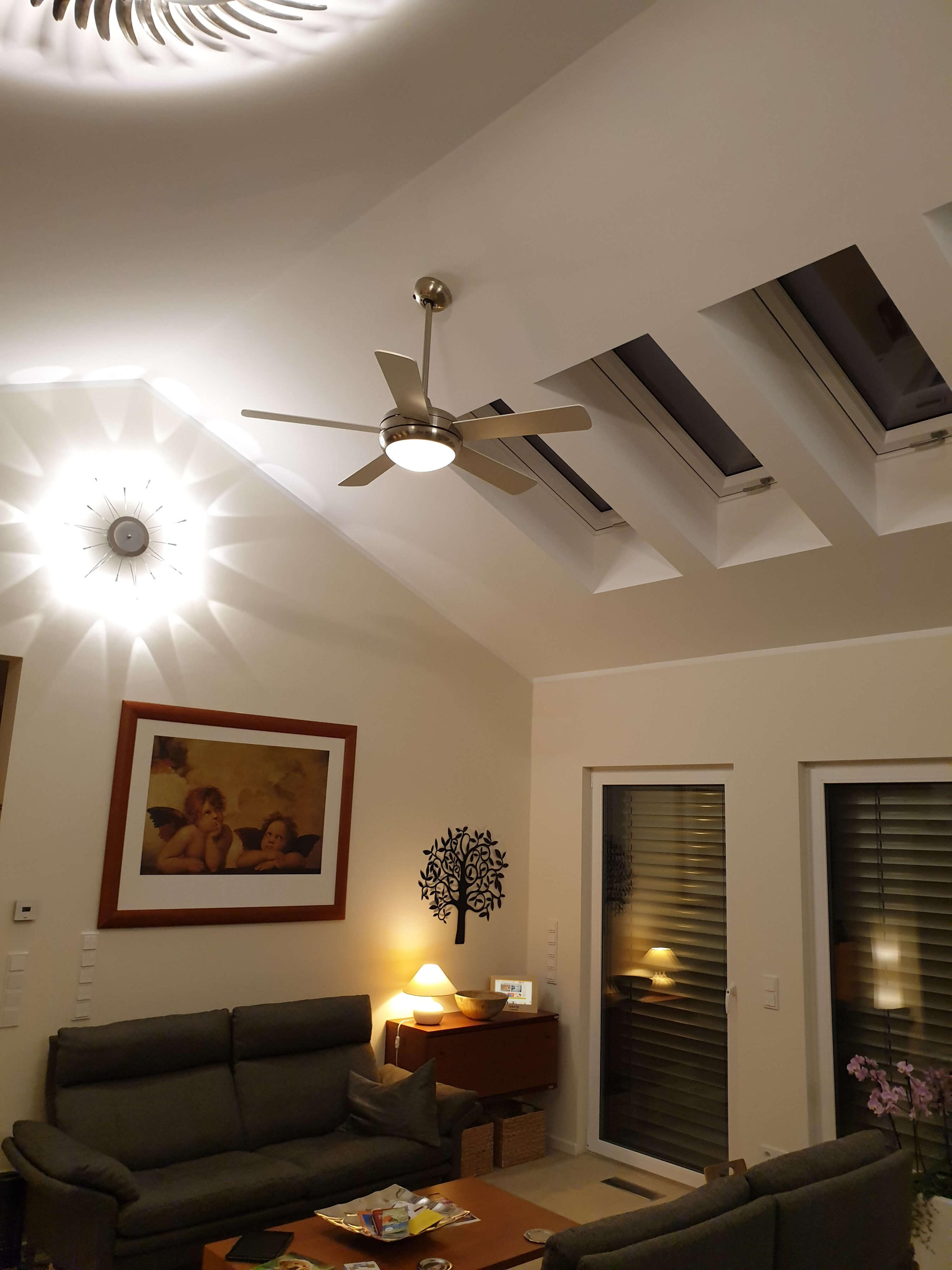 Wohnzimmer. Deckenventilator, gerahmte Kunst, Sofa und Fenster. Warme Beleuchtung.