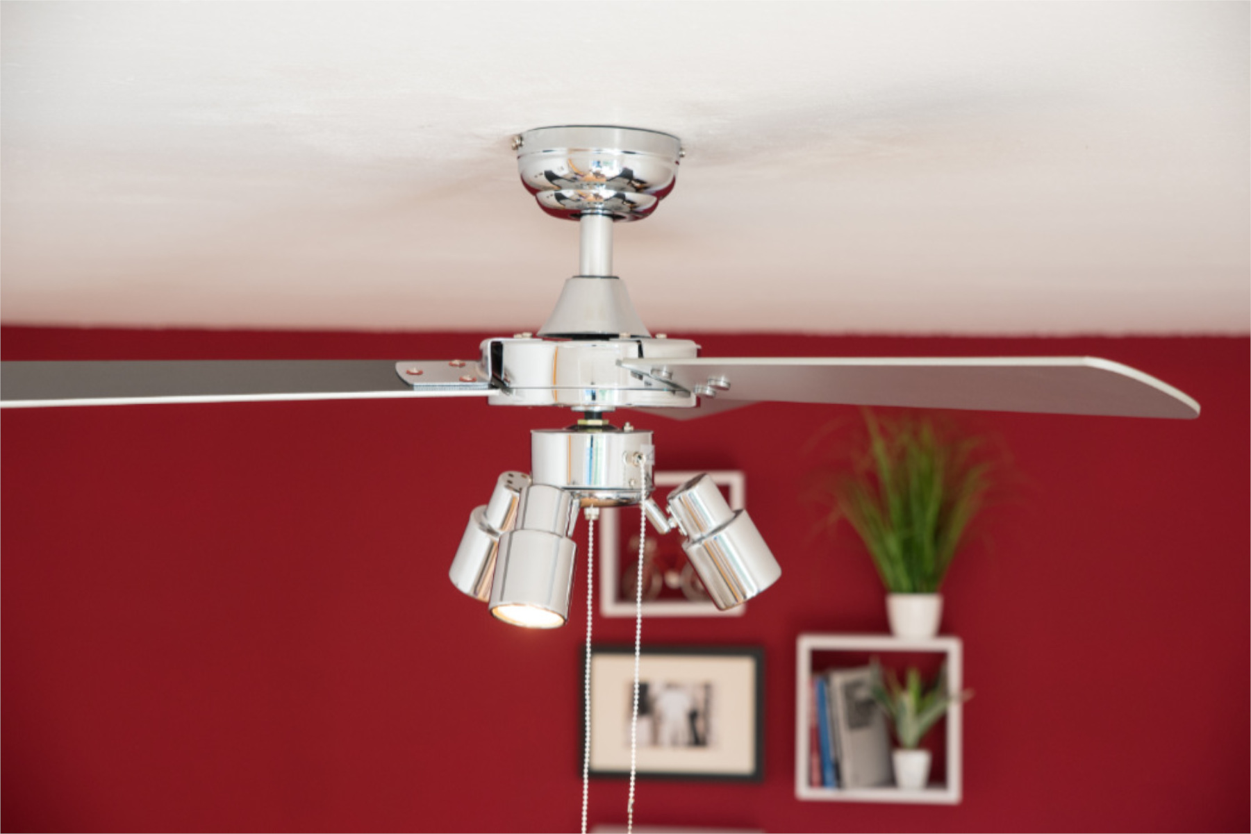 Ein Deckenventilator mit Lichtern. Rote Wand im Hintergrund.