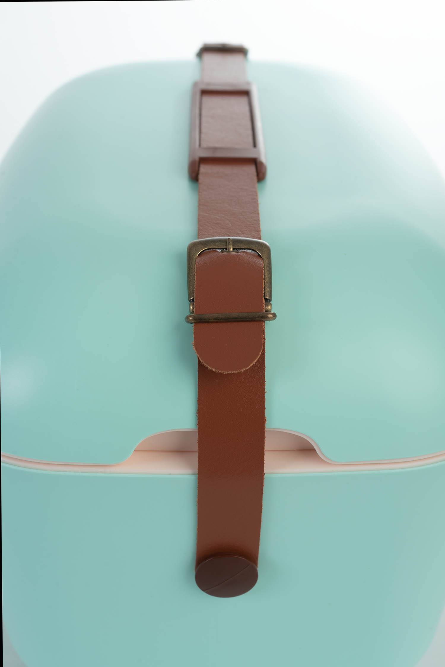Una valigia da viaggio verde menta con un cinturino e fibbia in pelle marrone, su sfondo bianco.