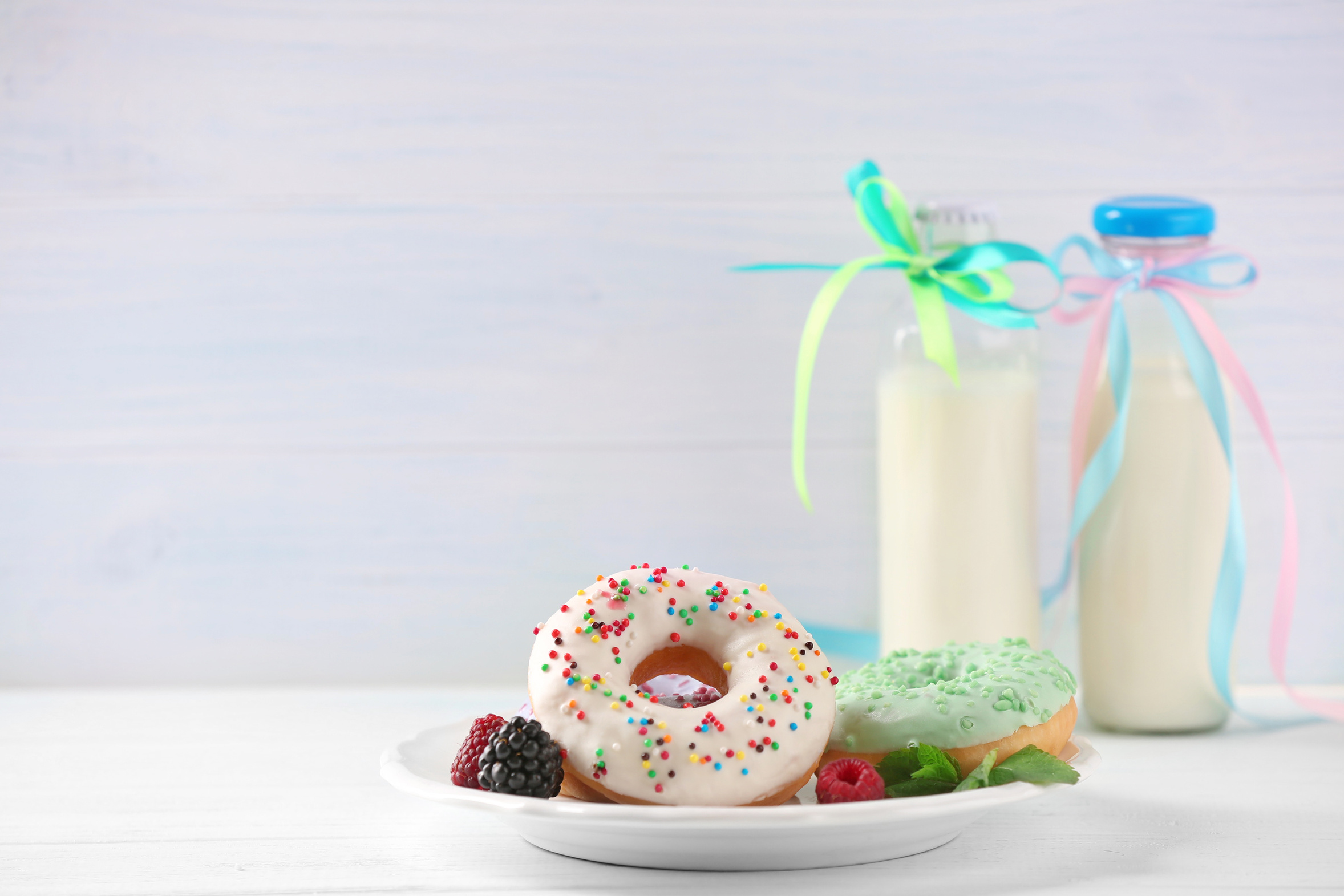 Talerz z pączkiem i jeżyną. Dwie butelki mleka z wstążkami.