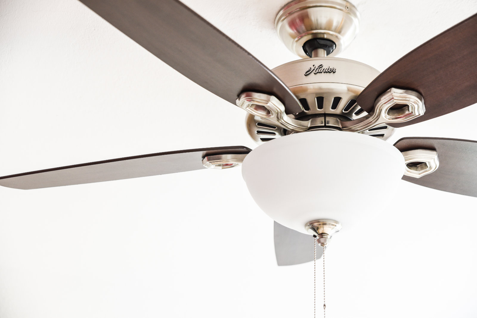 Ein Deckenventilator mit dunkelbraunen Flügeln und einer weißen Leuchte und Gehäuse.