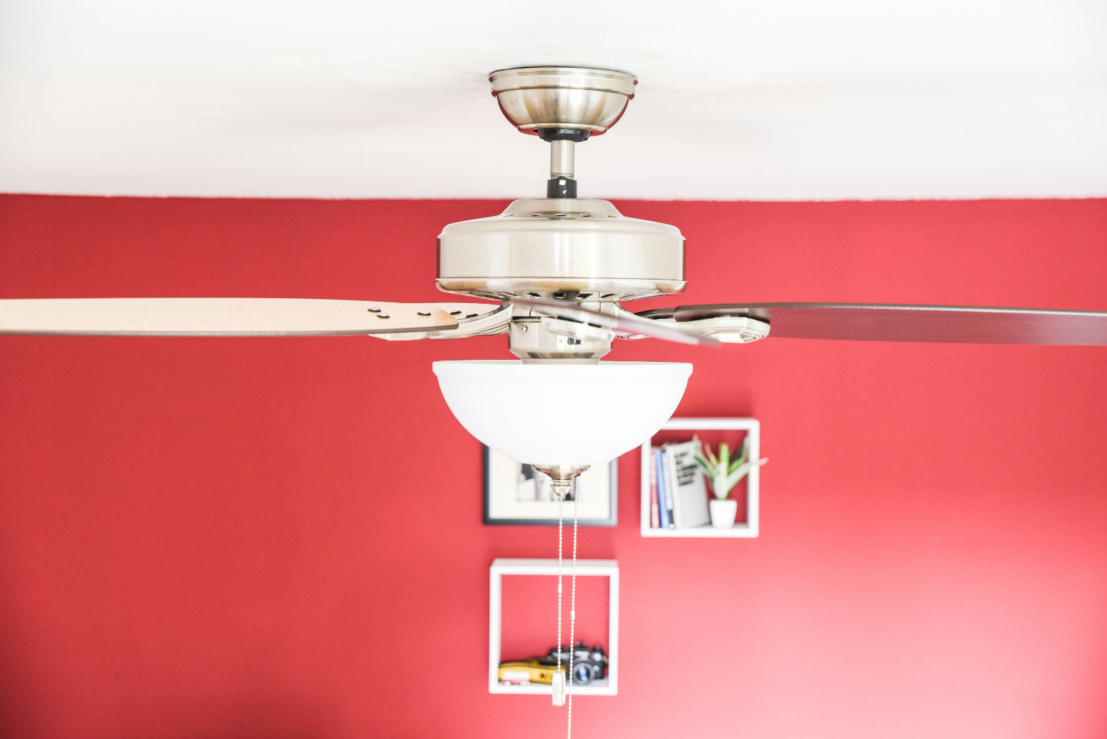 Deckenventilator mit einer darunter hängenden Leuchte. Rote Wand, weiße Regale und eine rote Wand.