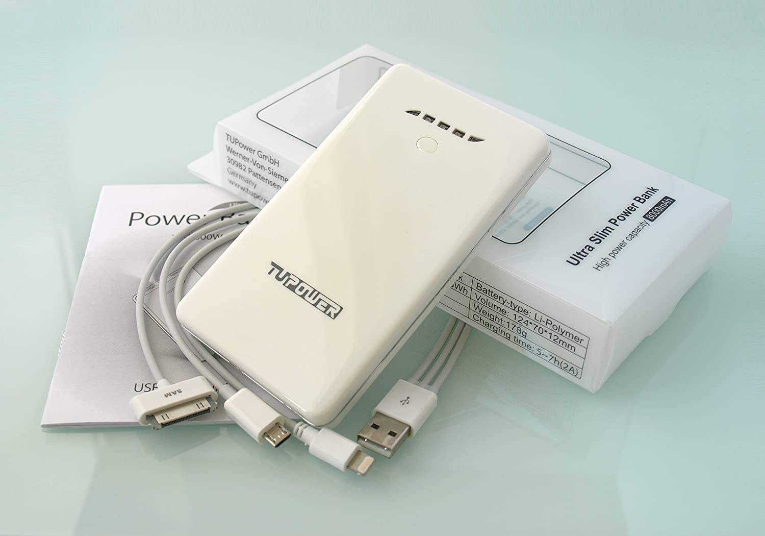 Eine weiße TUPOWER Powerbank mit Kabeln und Verpackung auf reflektierender Oberfläche.
