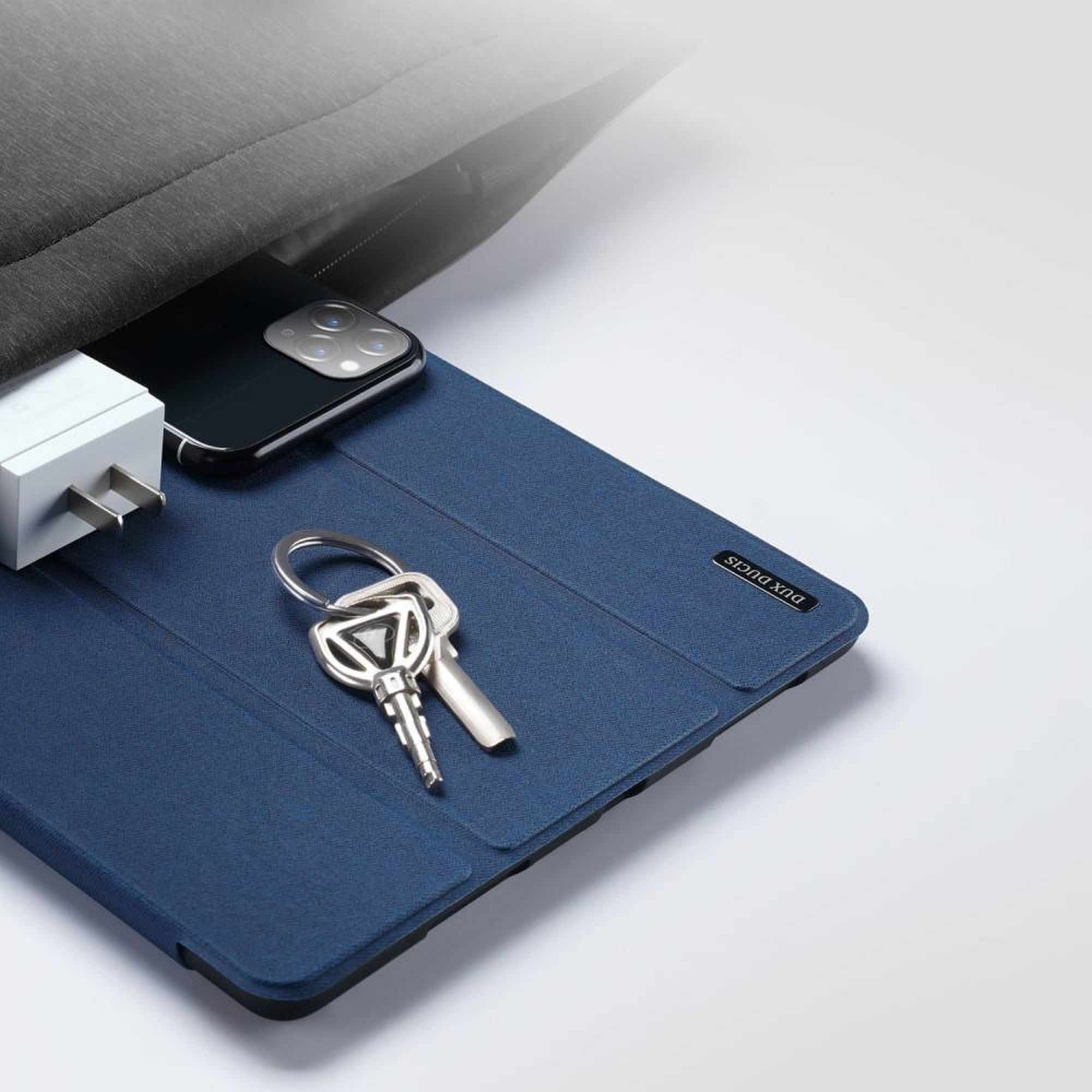 Telefon, Schlüssel und Ladegerät auf blauem Tablet-Etui. Tasche teilweise sichtbar.