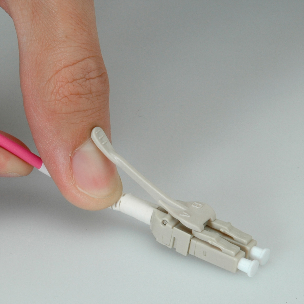 Een hand die een witte en roze connector vasthoudt. De connector is bevestigd aan een witte kabel.