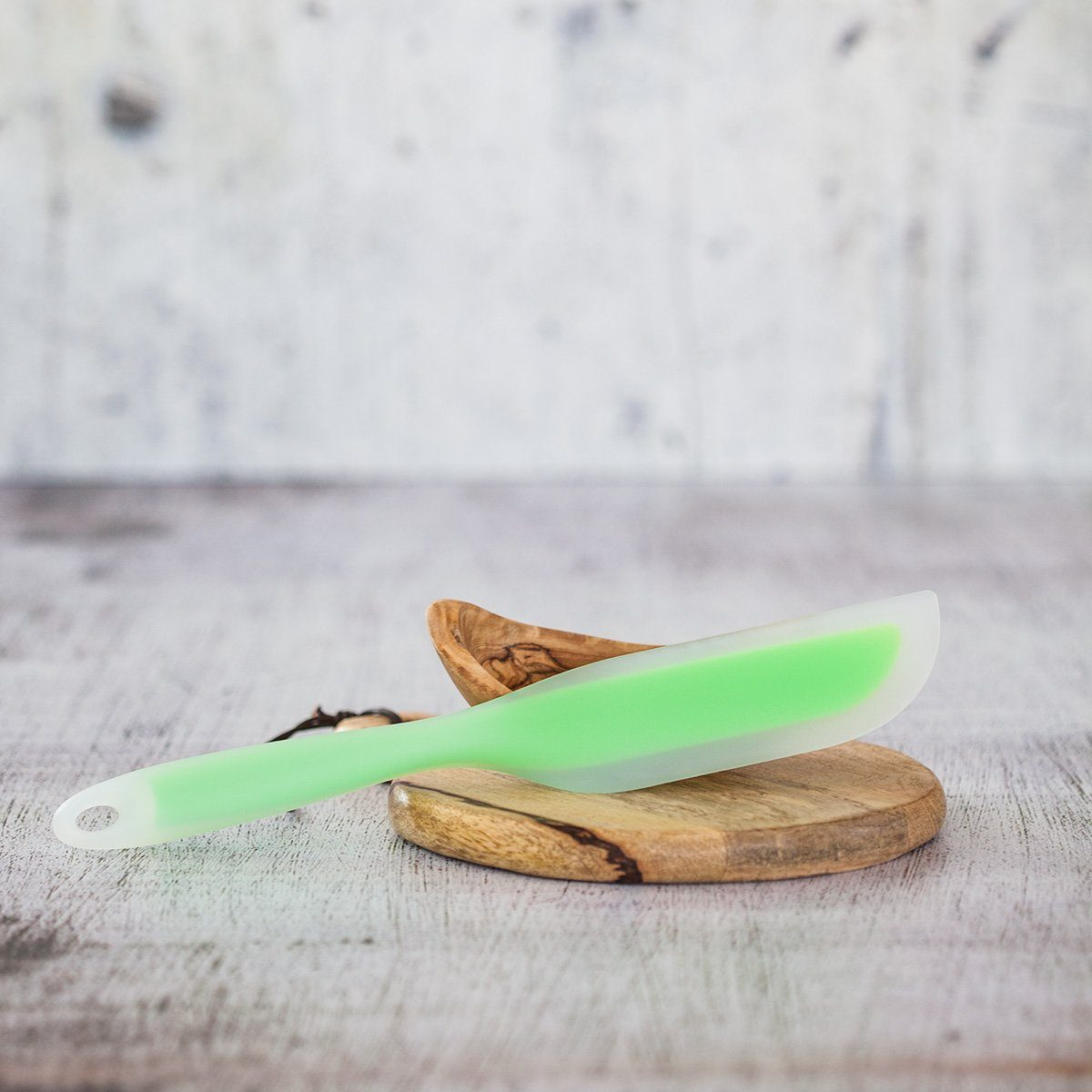 Spatola verde su un tagliere in legno, posta su uno sfondo leggermente sfocato.