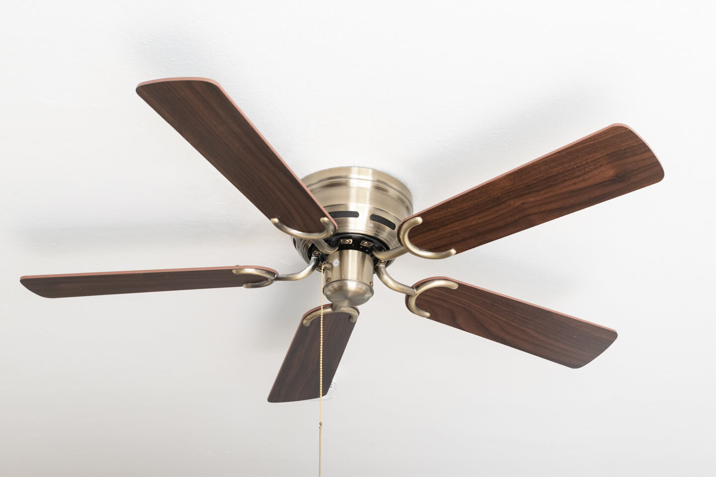 Deckenventilator mit braunen Flügeln und messingfarbenem Motor. Der Ventilator ist zentriert.