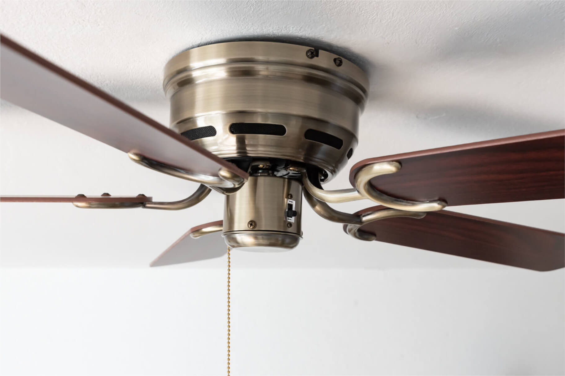 Nahaufnahme eines Deckenventilators mit Holzflügeln und Messingausführung.