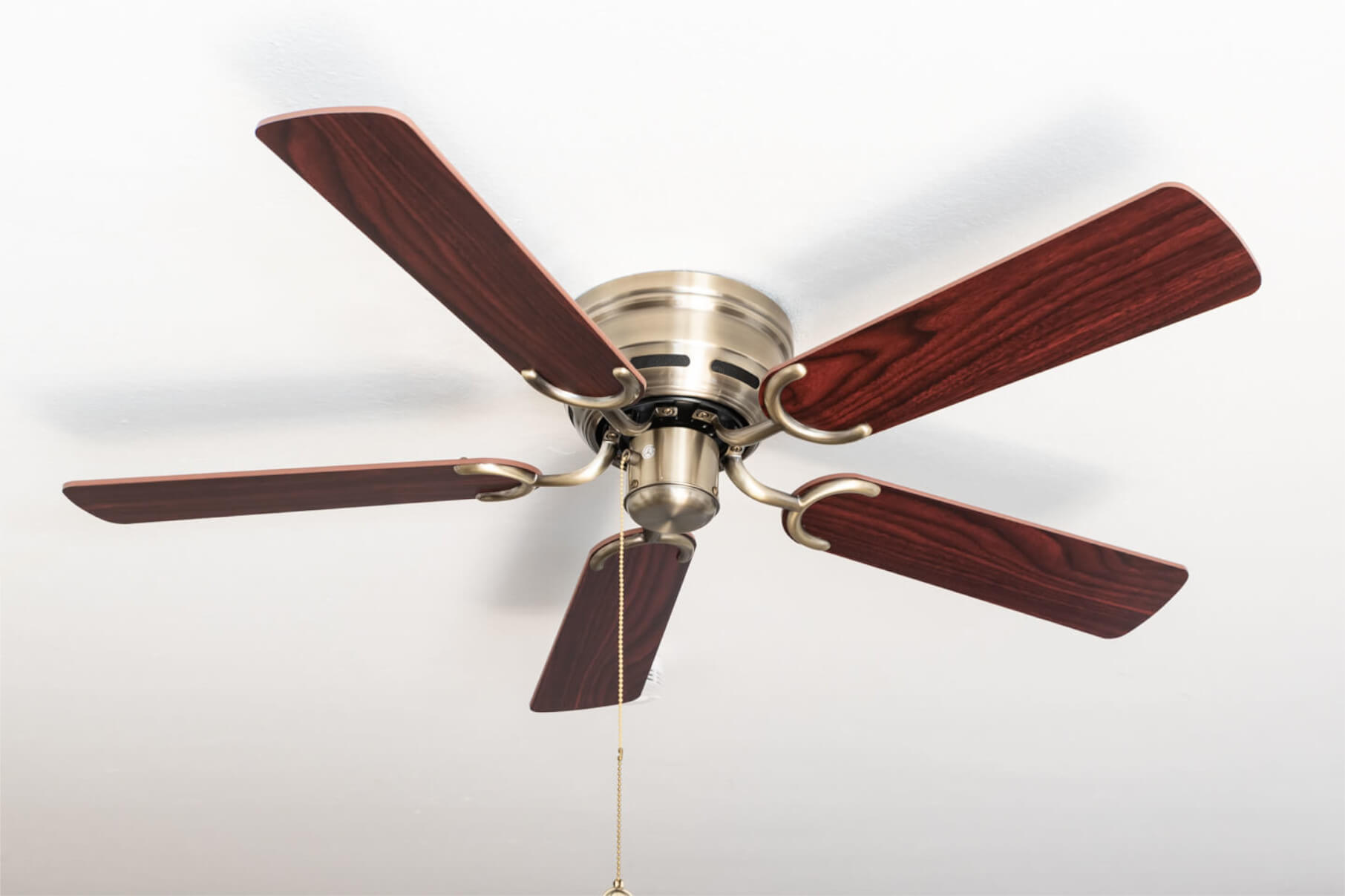 Deckenventilator mit fünf Holzflügeln, Bronzemotor und weißem Deckenhintergrund.