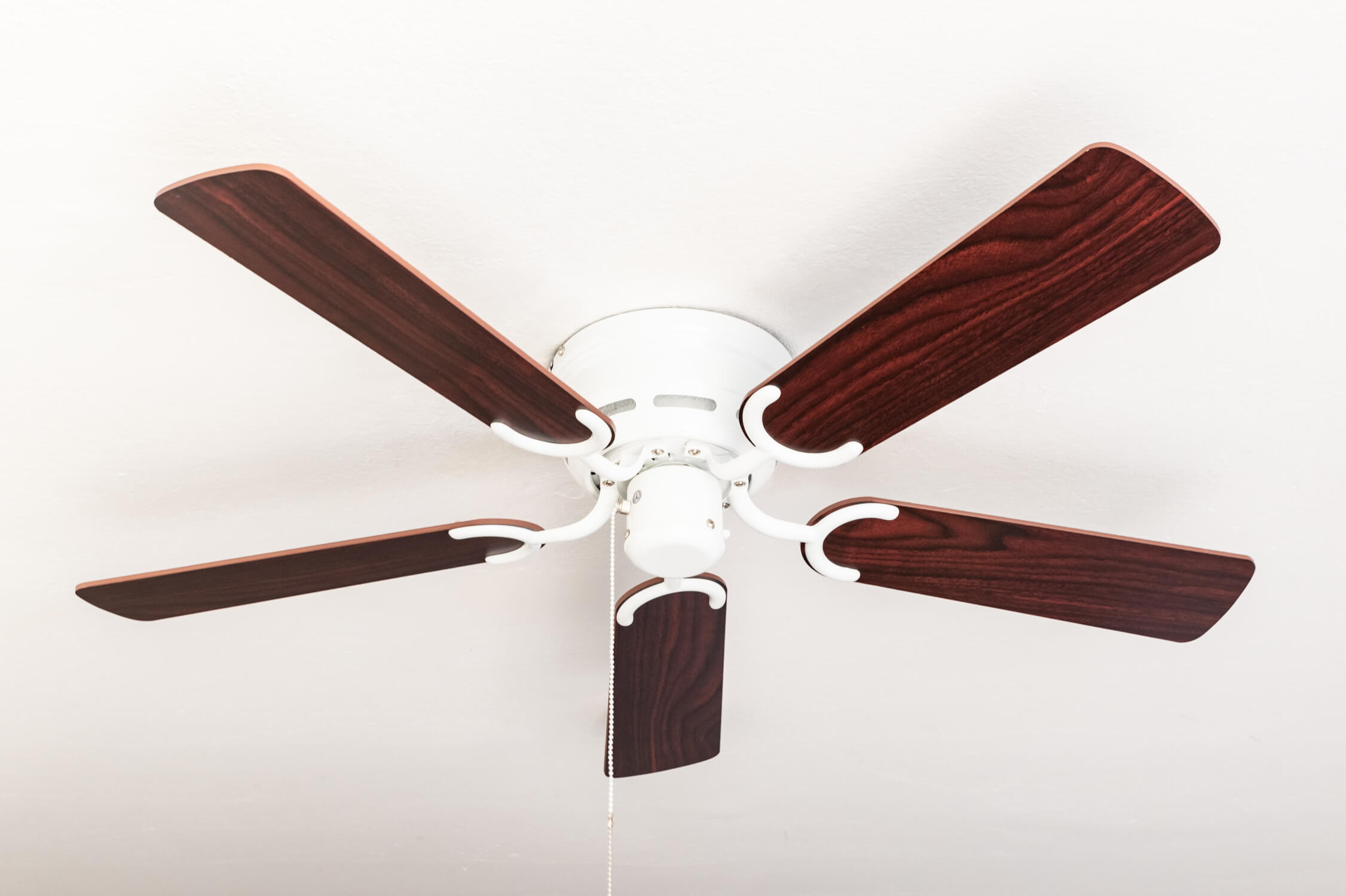 Deckenventilator mit fünf Holzblättern und weißem Motorgehäuse, an einer weißen Decke montiert.