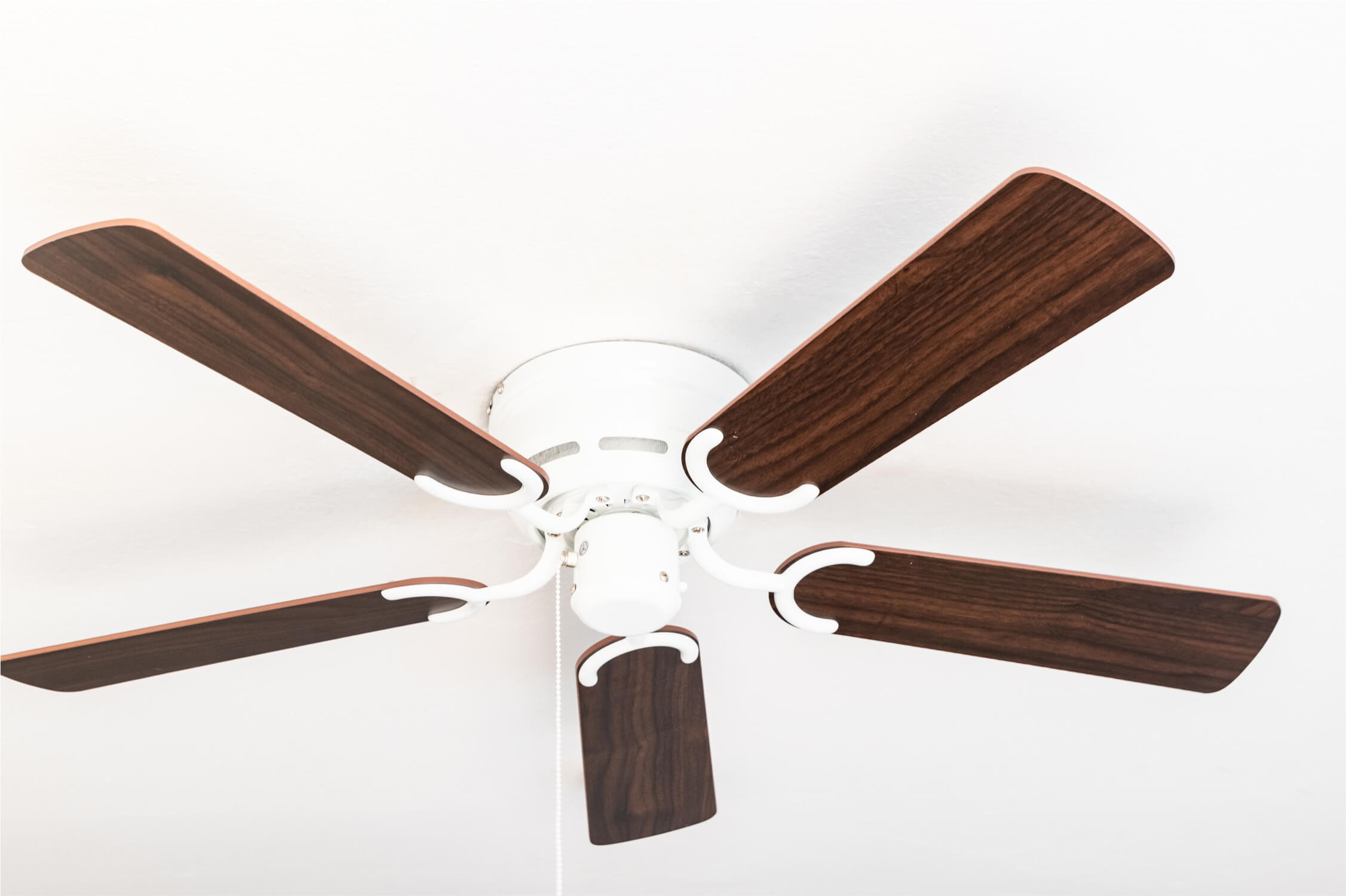 Deckenventilator mit fünf dunklen Holzblättern und einem weißen Motorgehäuse.