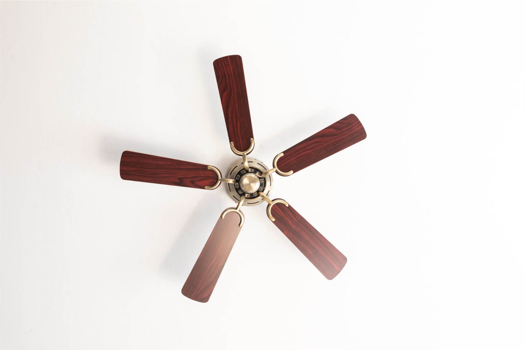 Deckenventilator mit fünf Flügeln, Holzmaserung. Die Flügel sind braun, zentriert an weißer Decke.
