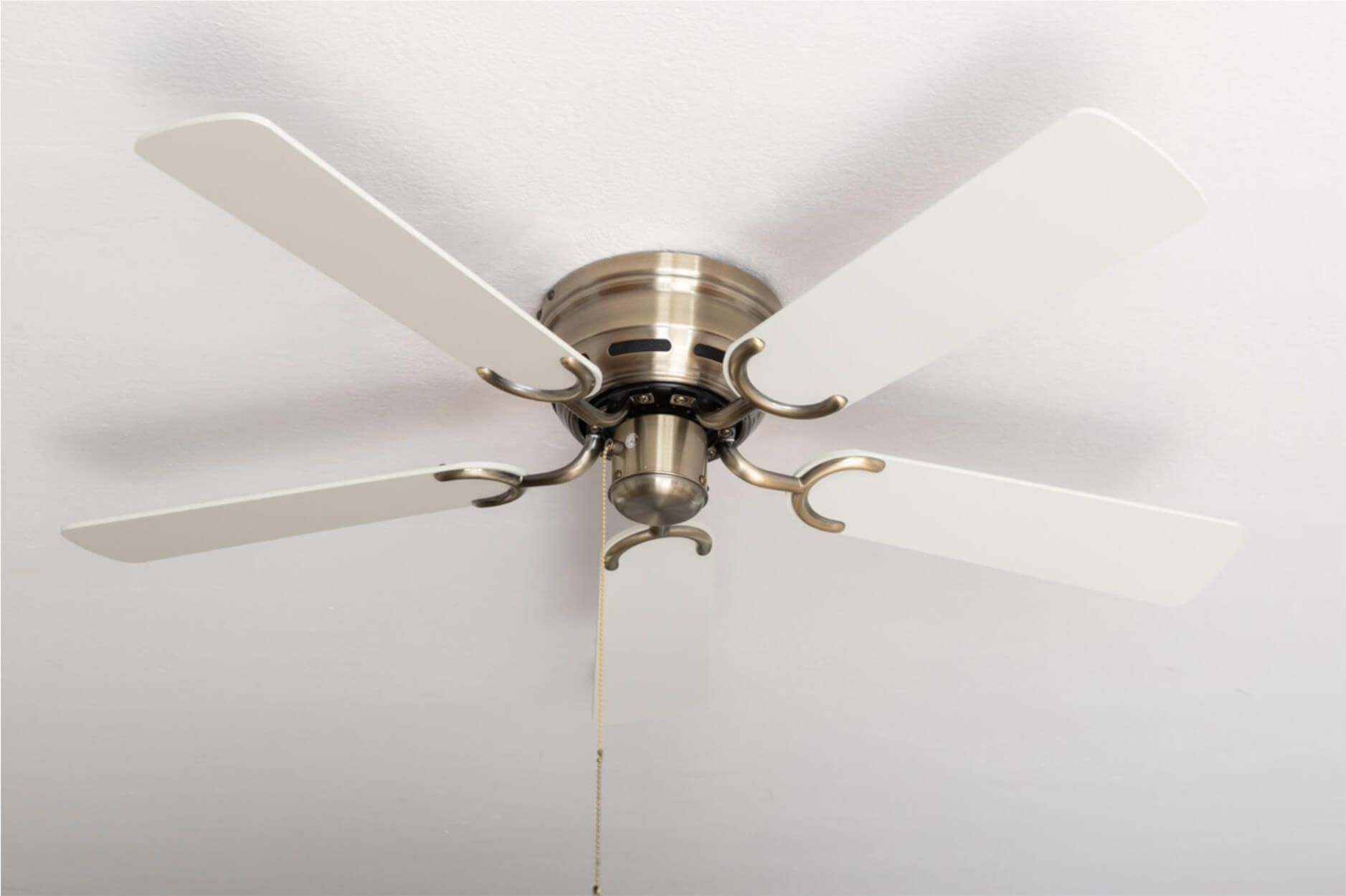 Deckenventilator mit Messingarmatur und weißen Flügeln vor weißer Decke.