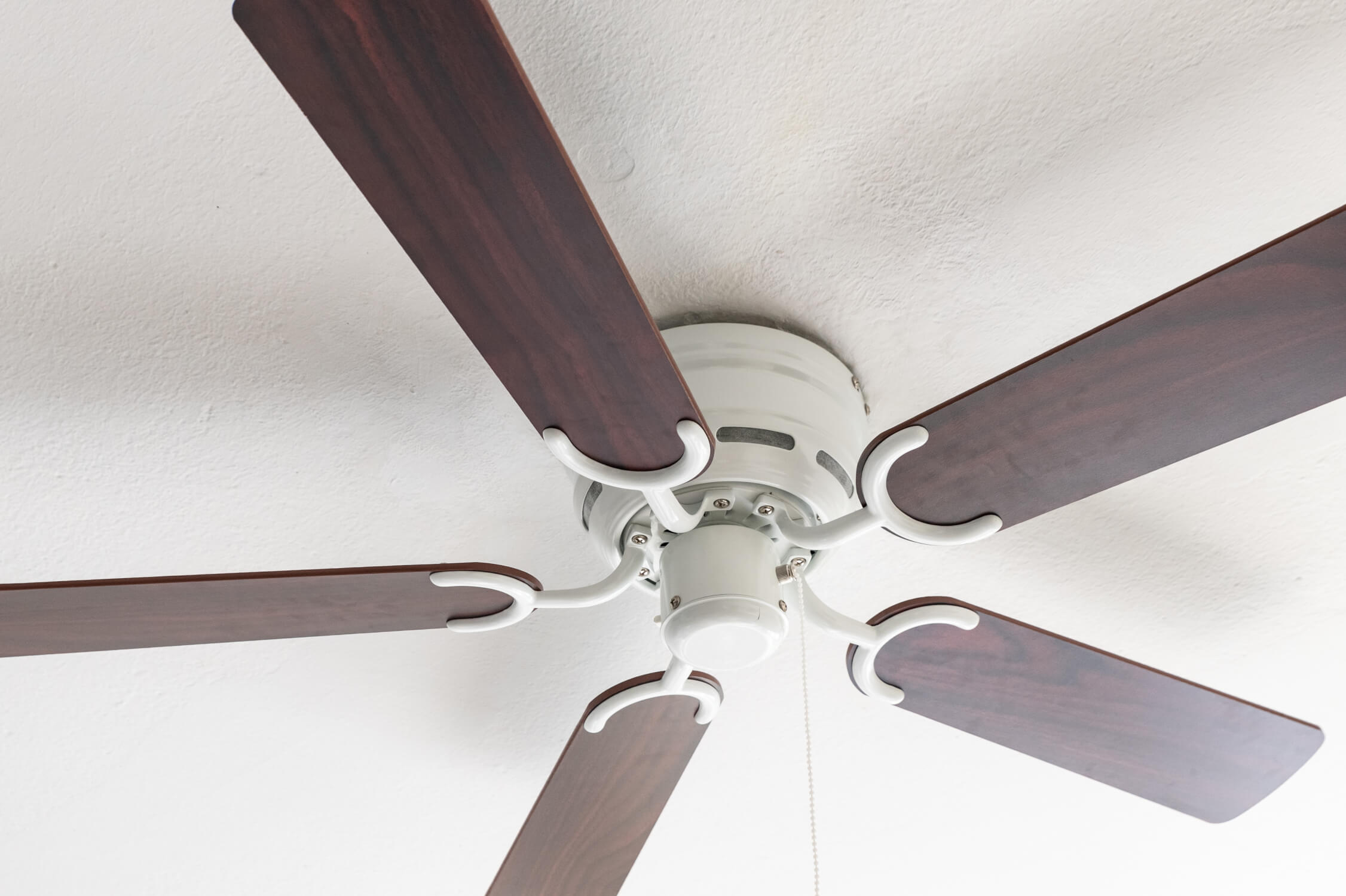 Deckenventilator mit fünf dunklen Holzblättern, weißem Motorgehäuse und weißen Armen.