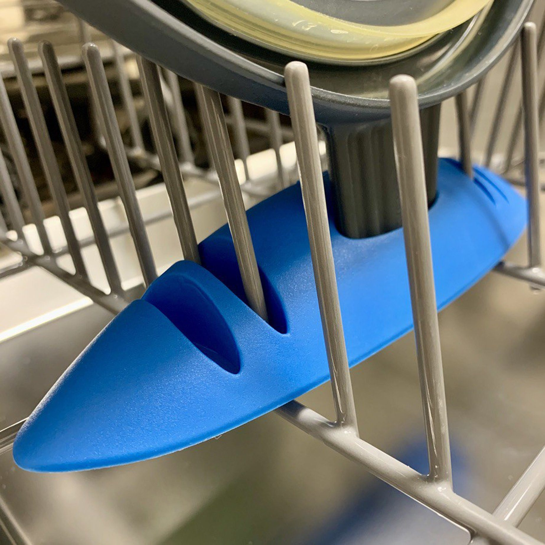 Un utensile di plastica blu in un cestello per lavastoviglie, con fili del cestello sullo sfondo.