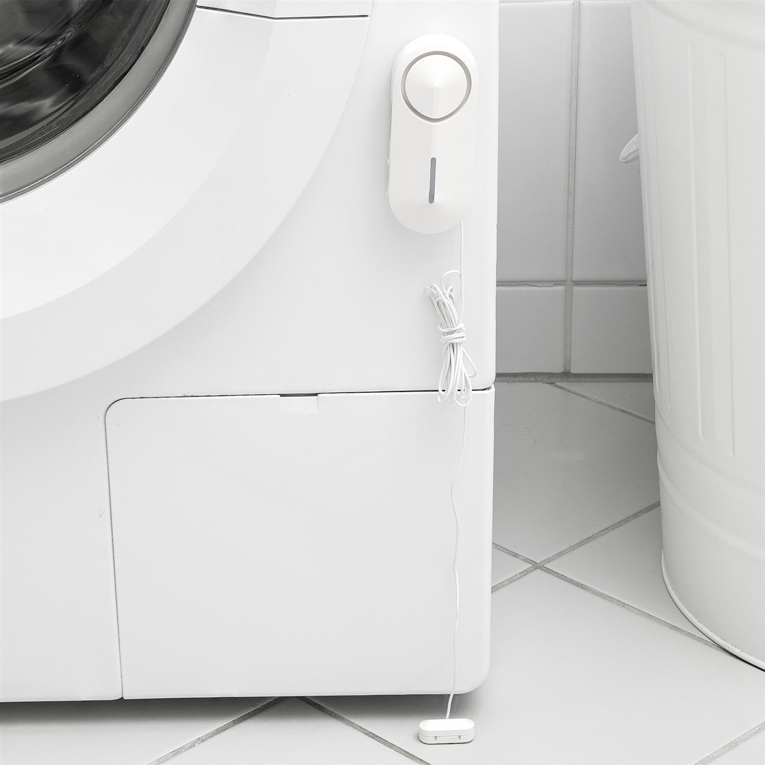 Weiße Waschmaschine mit einem daran befestigten weißen Sensor, neben einem weißen Mülleimer.
