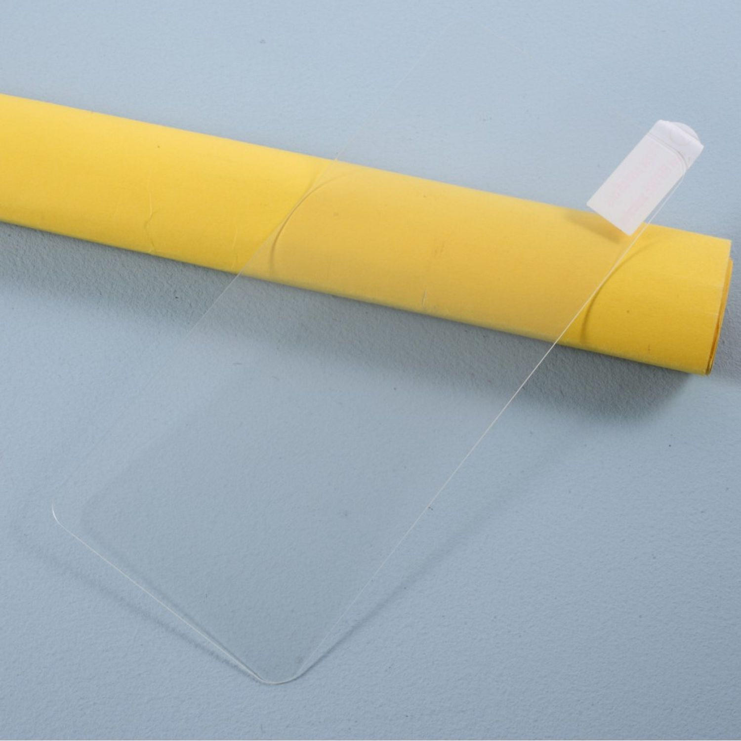 Ein transparenter Displayschutz wird von einer gelben Rolle abgezogen, auf einer blauen Oberfläche.