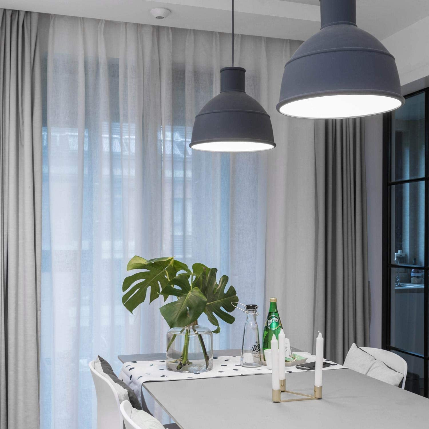 Lampade a sospensione grigie sopra un tavolo da pranzo con monstera e candele.