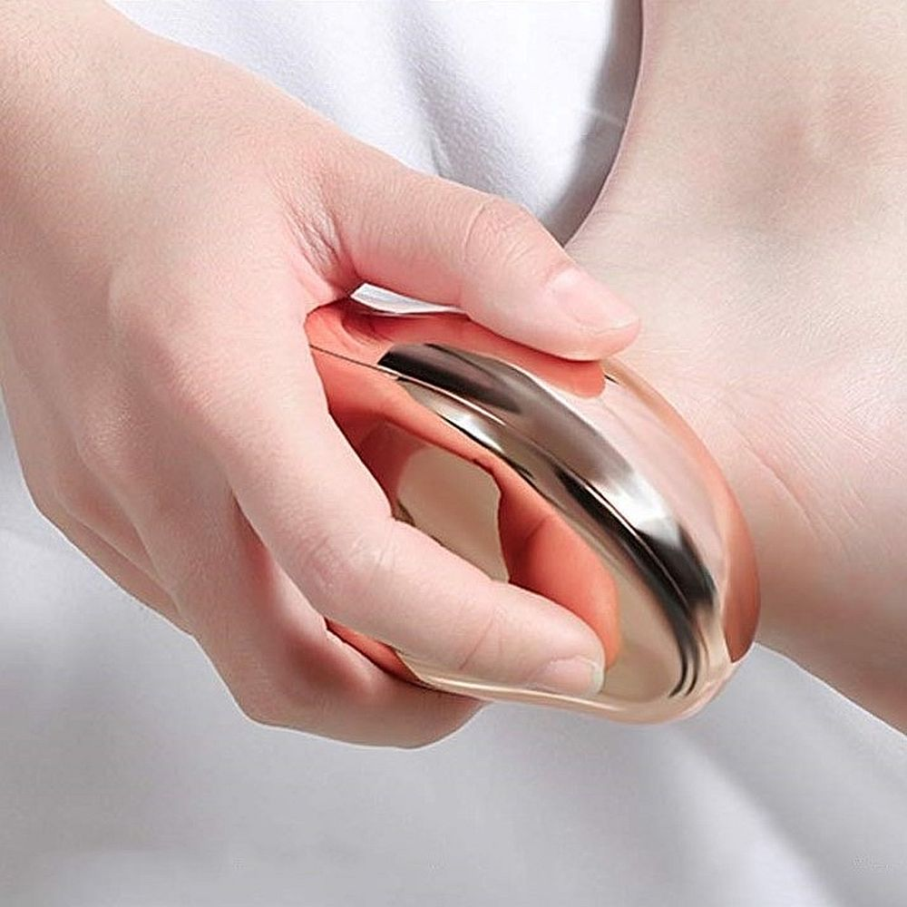 Eine Hand hält ein bronzefarbenes Fußmassagegerät.