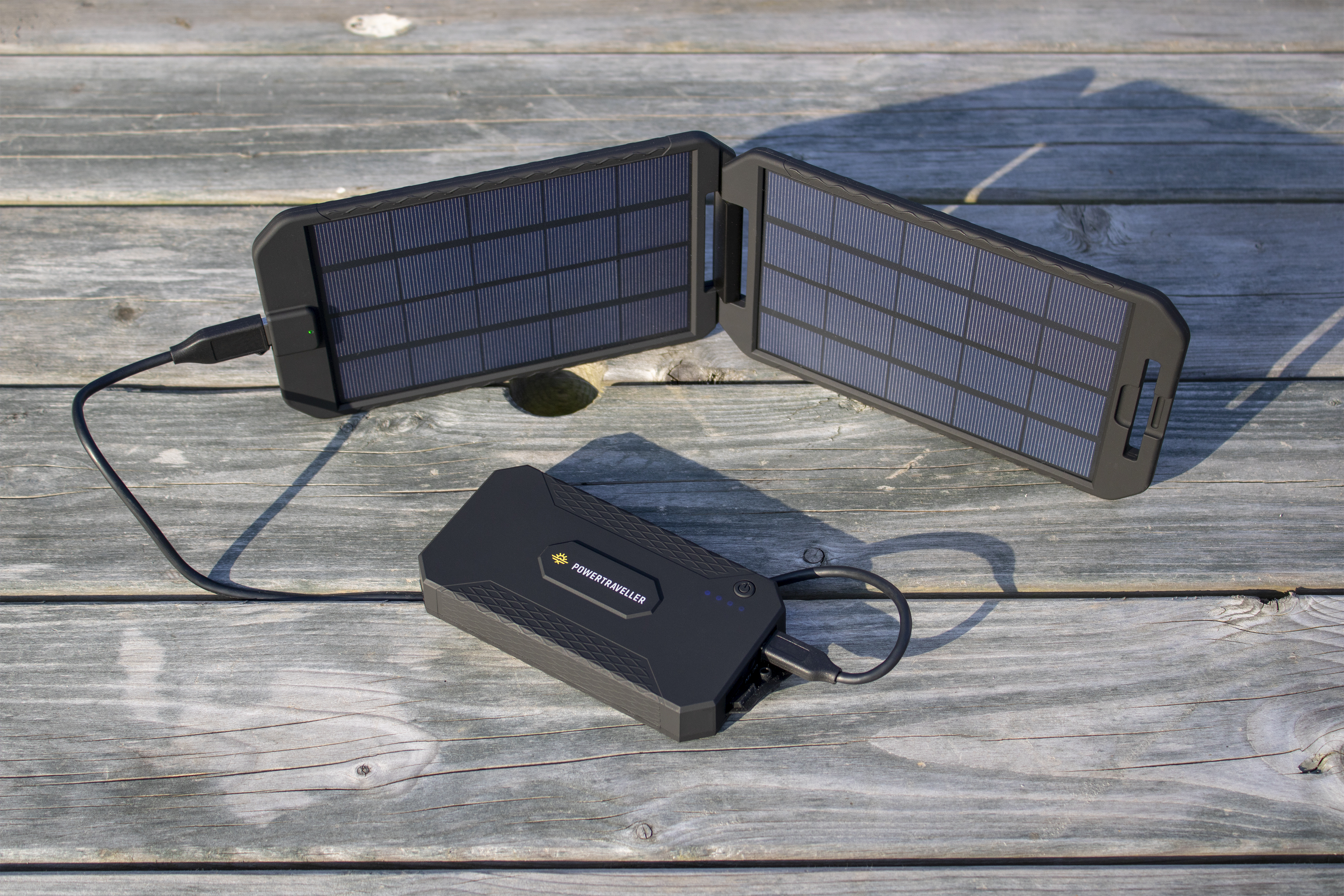 Ein tragbares Solarladegerät mit zwei Paneelen und einer schwarzen Ladeeinheit auf Holz.