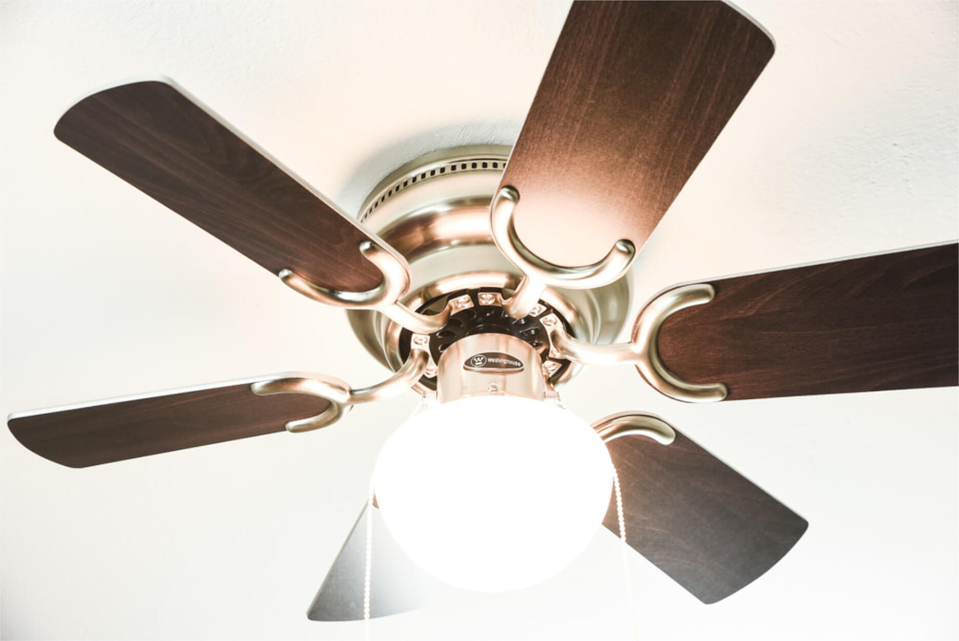 Deckenventilator mit dunklen Holzflügeln und einer Lichtvorrichtung. Er ist silber und weiß.