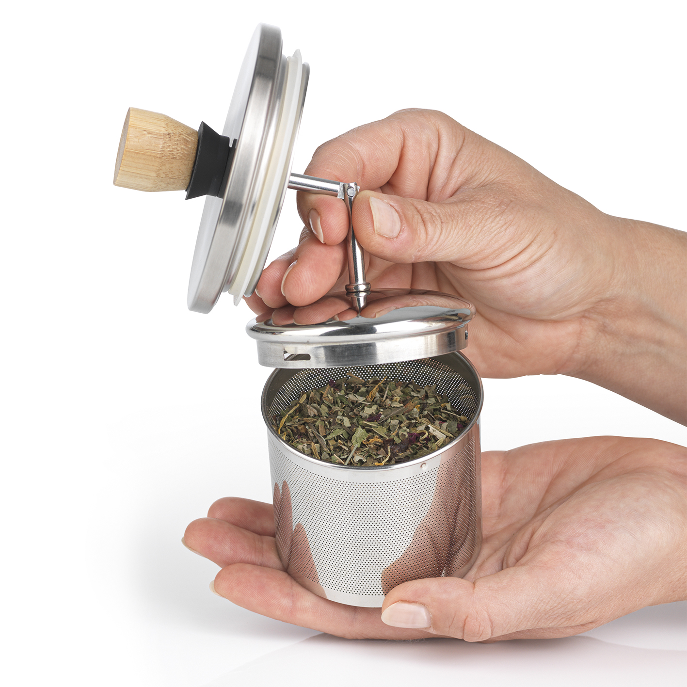 Hände halten einen silbernen Tee-Infuser. Er ist geöffnet und zeigt getrocknete Kräuter.
