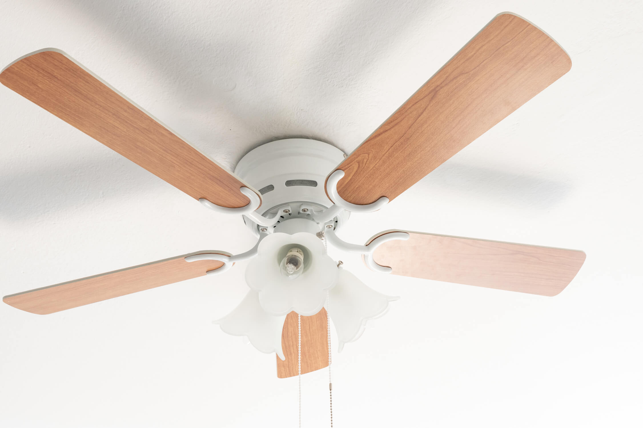 Ventilatore da soffitto con quattro pale in legno e base bianca, su un soffitto bianco.