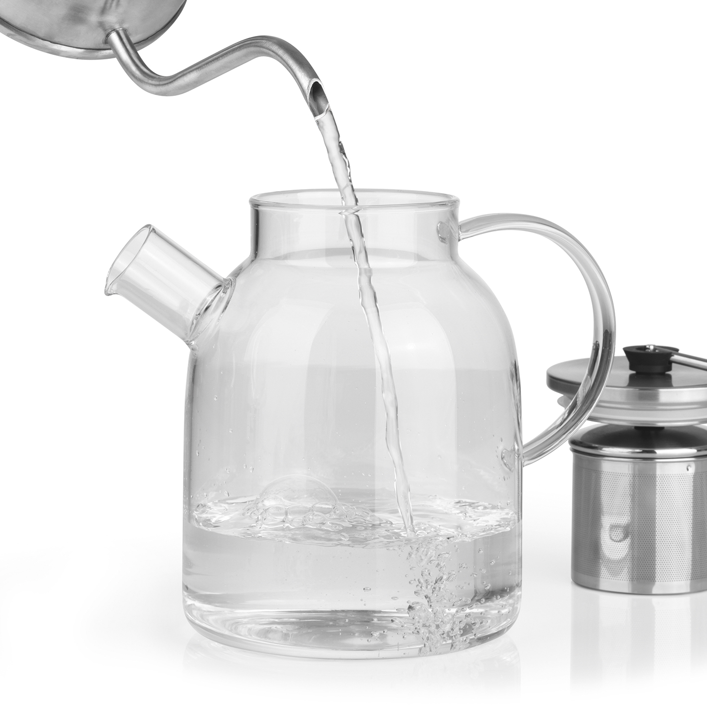 Wasser gießt in eine gläserne Teekanne. Daneben befindet sich ein Tee-Sieb aus Metall.