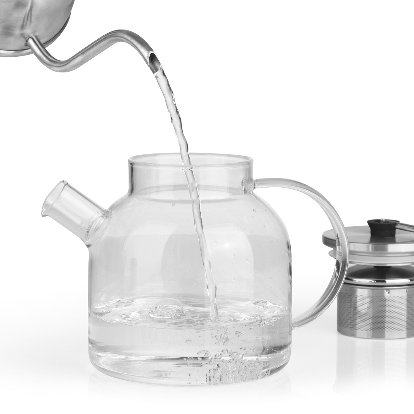 Wasser, das aus einem silbernen Ausguss in eine klare Glaskanne mit Metall-Infuser gegossen wird.