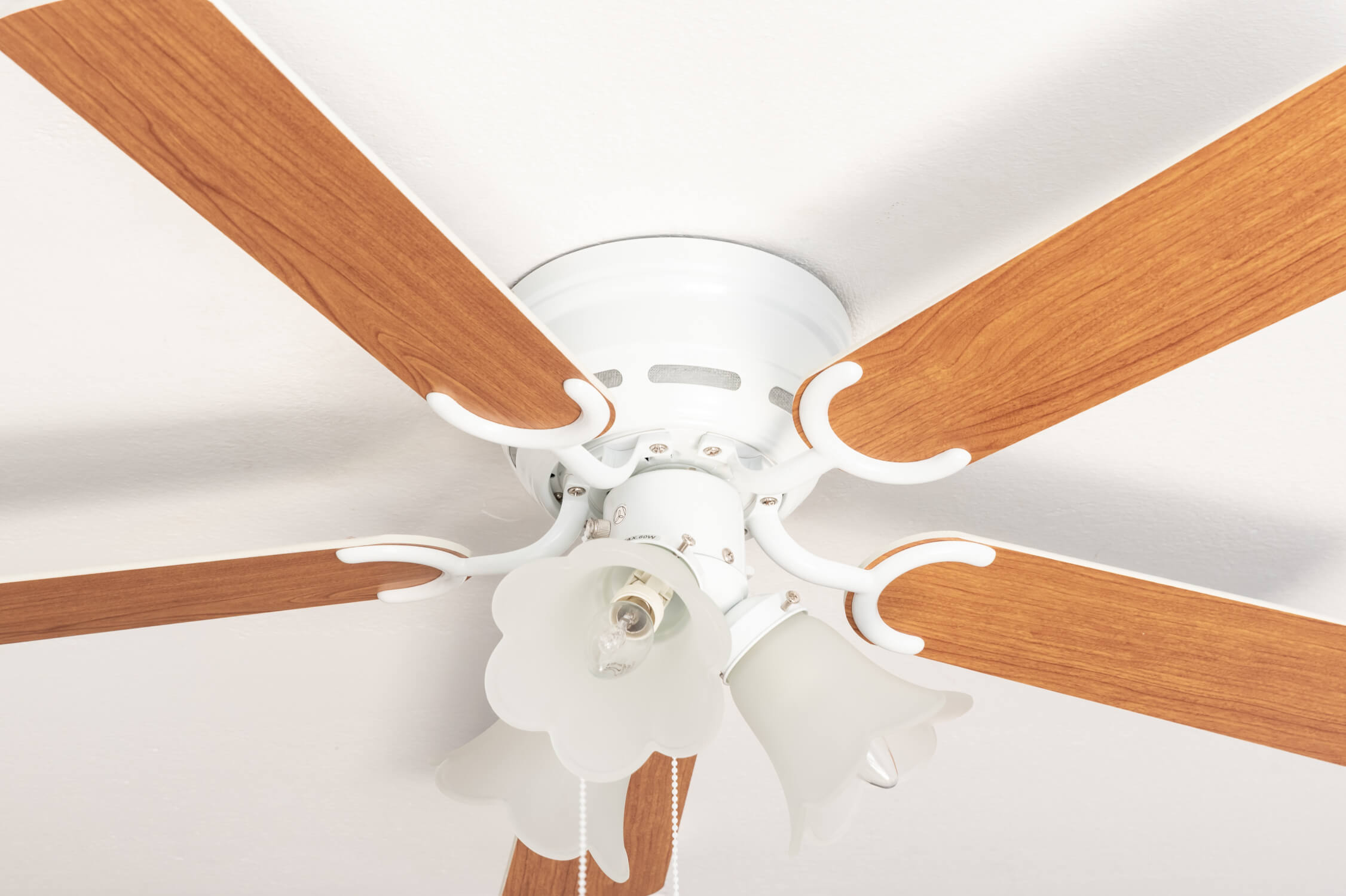 Un ventilatore da soffitto bianco con pale in legno e un'apparecchio di illuminazione decorativo visto dal basso.