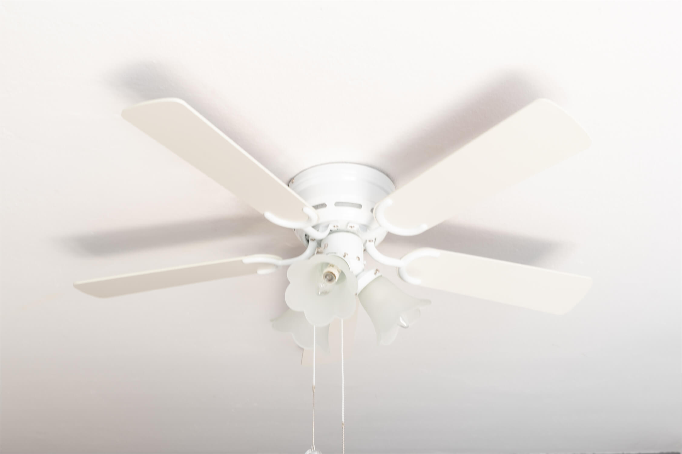 Un ventilatore da soffitto bianco con cinque pale e un'apparecchio di illuminazione, ombre sul soffitto bianco.