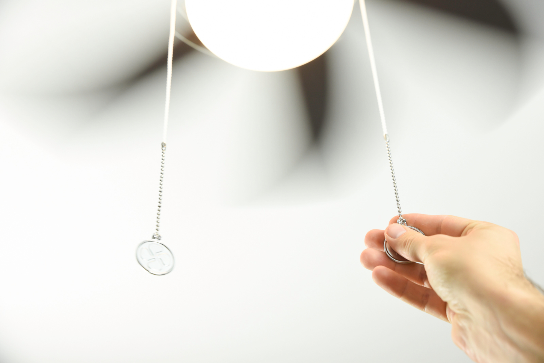 Eine Hand zieht an einer Deckenventilator-Kette. Der Ventilator ist verschwommen, weiße Decke. Silberkette mit Metallzug.