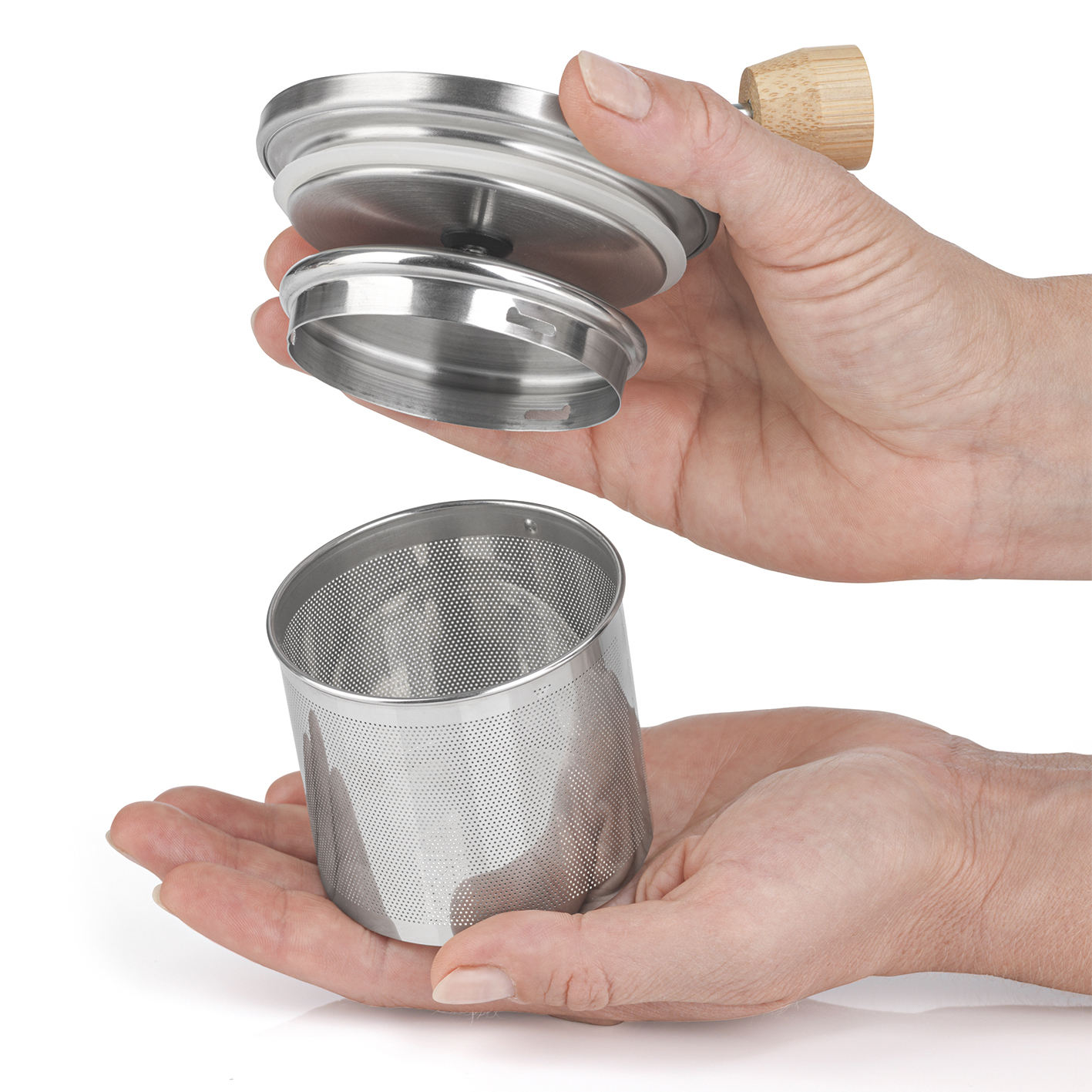 Hände halten Tee-Infuser. Der Deckel hat einen Holzgriff, der Infuser ist ein Metallgitter.