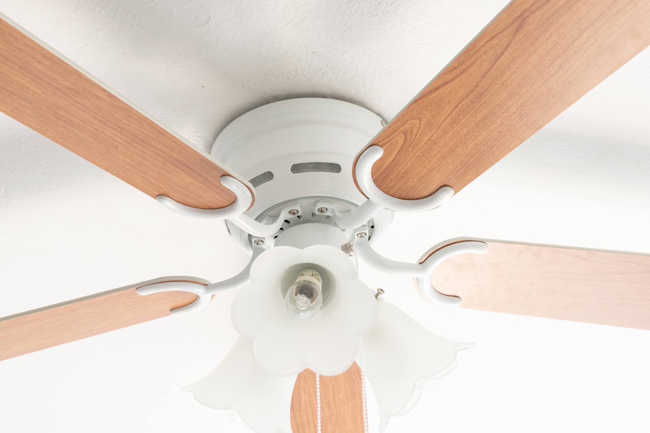 Ventilatore a soffitto con pale effetto legno, apparecchio bianco e luce decorativa.
