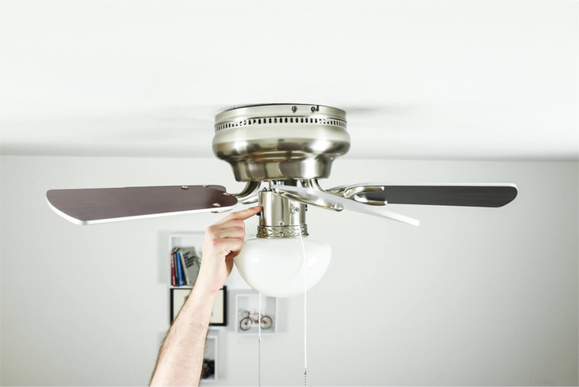 Hand einer Person, die einen Deckenventilator einstellt. Der Ventilator hat braune Flügel und eine Leuchte.